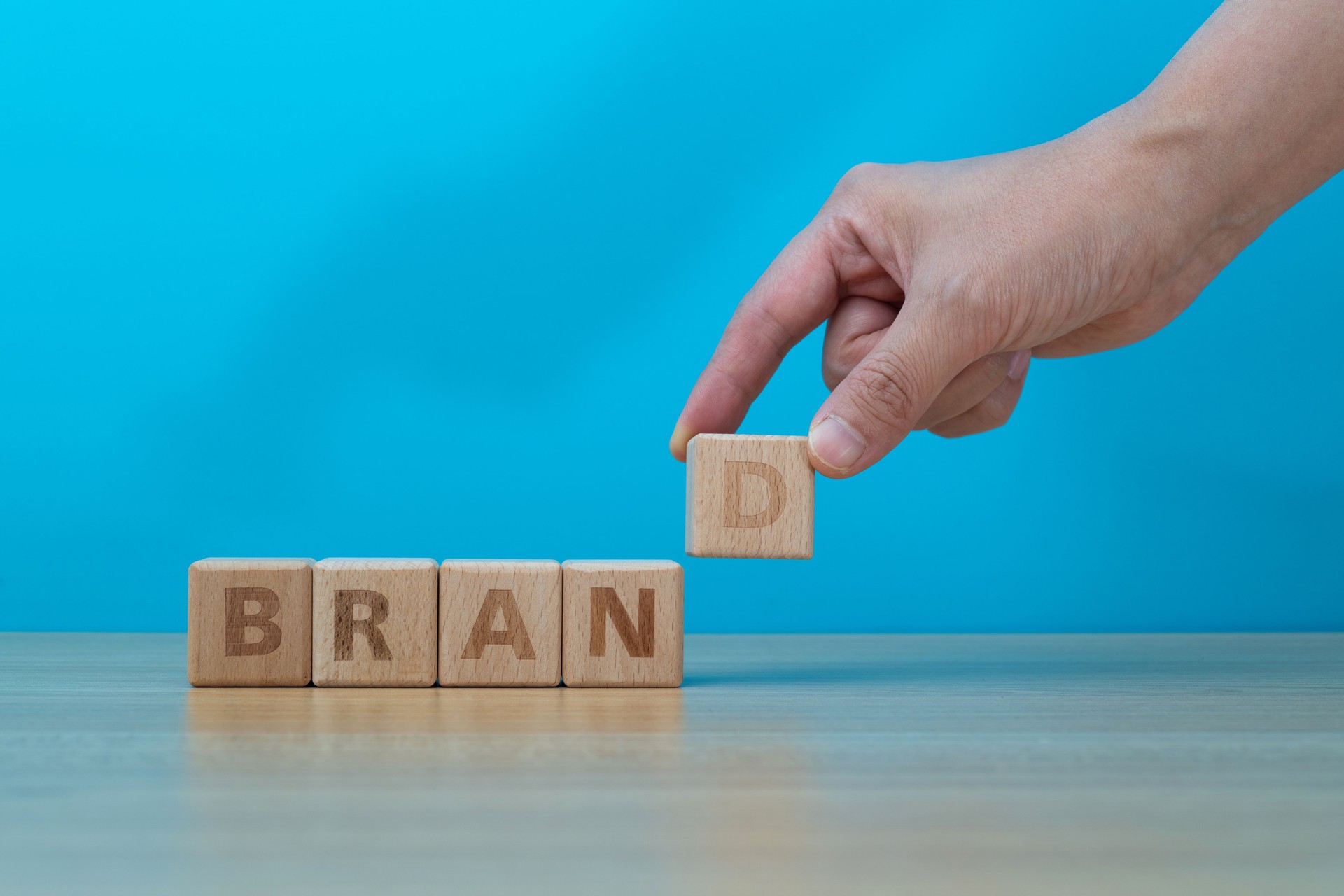 Human hand spelling word brand with toy blocks